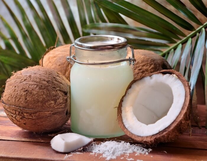 Coconut oil in a glass jar with coconuts and palm leaves in the background