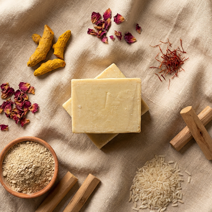 Three bars of soap on a textured surface with turmeric, dried flowers, and other ingredients.